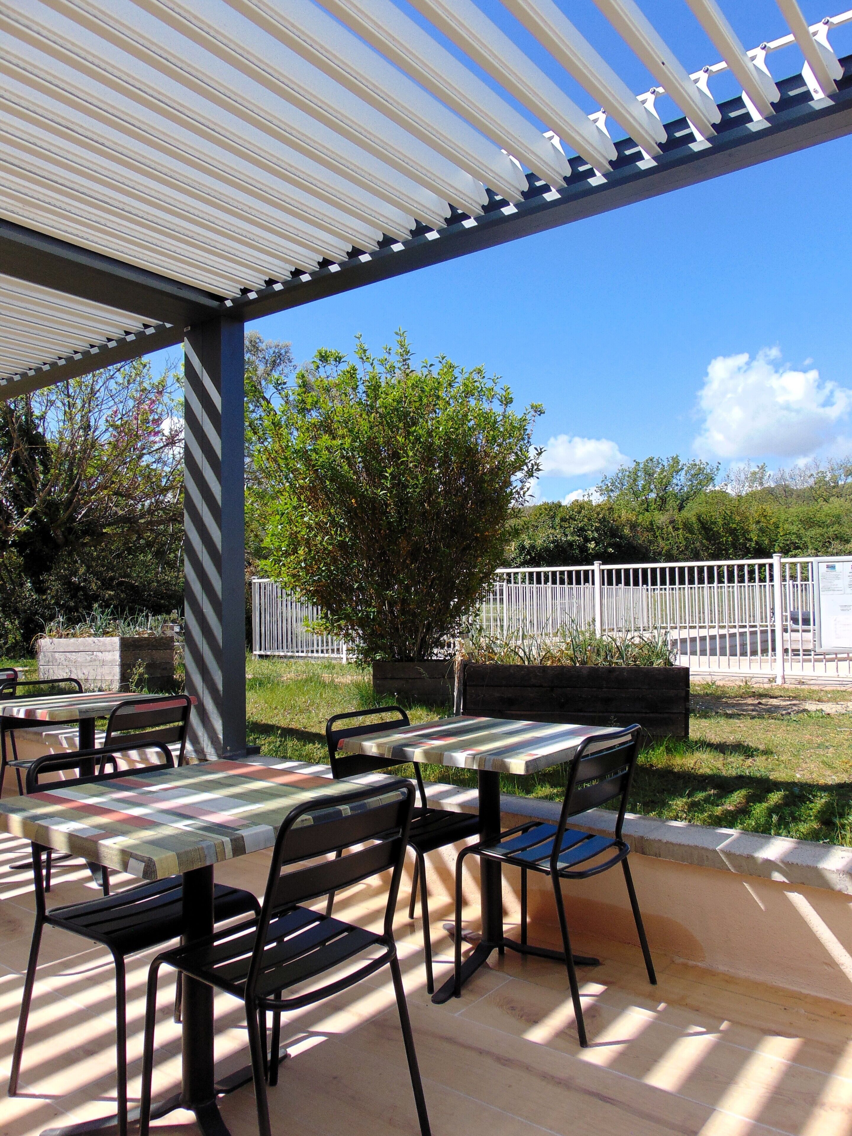 Un patio al aire libre con mesas y sillas, un área cubierta y vista a una cerca y árboles.