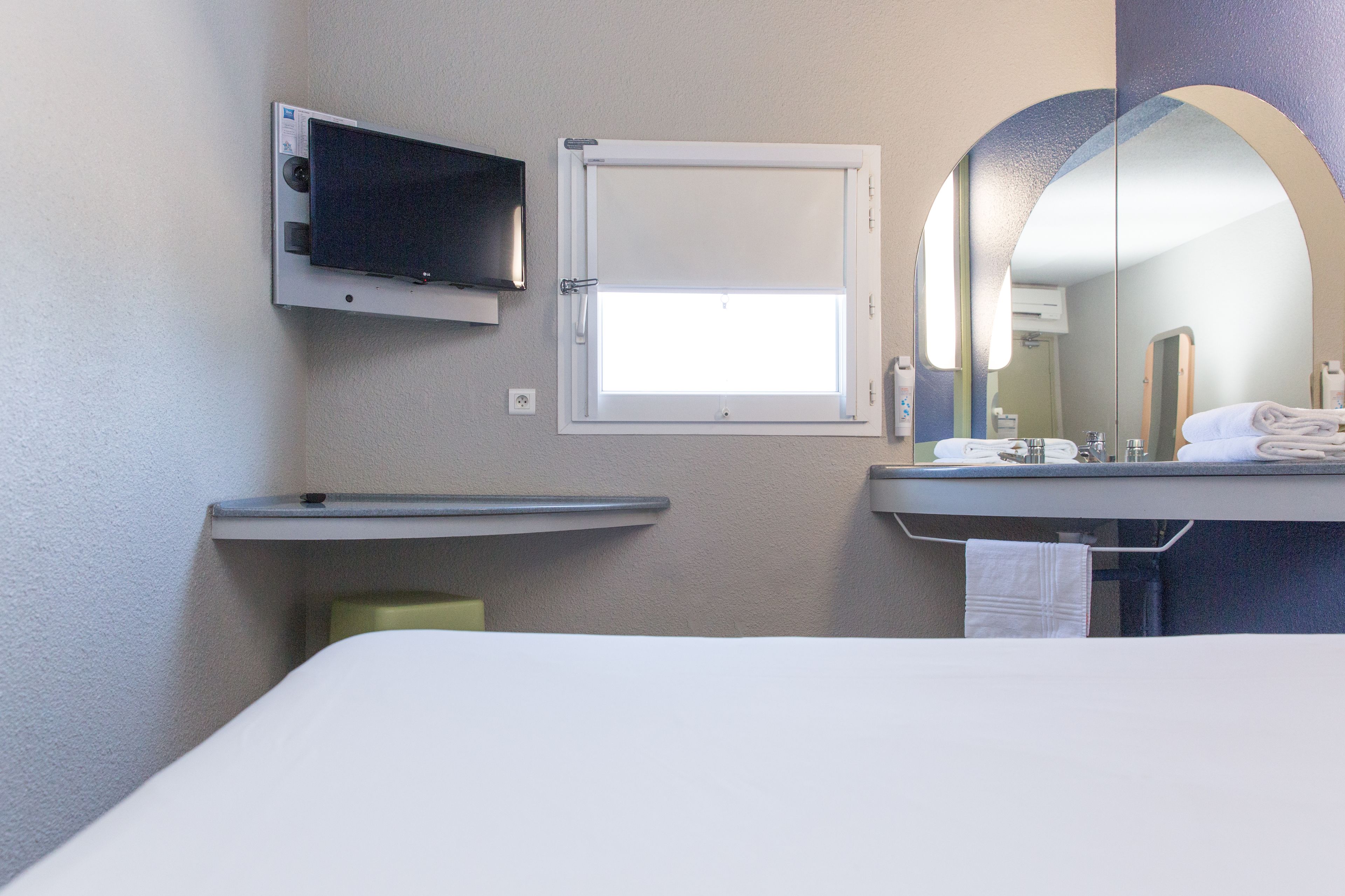 Une chambre d’hôtel avec un lit, un téléviseur fixé au mur, une fenêtre donnant sur un paysage agréable, un lavabo avec un miroir et une serviette suspendue au porte-serviettes.
