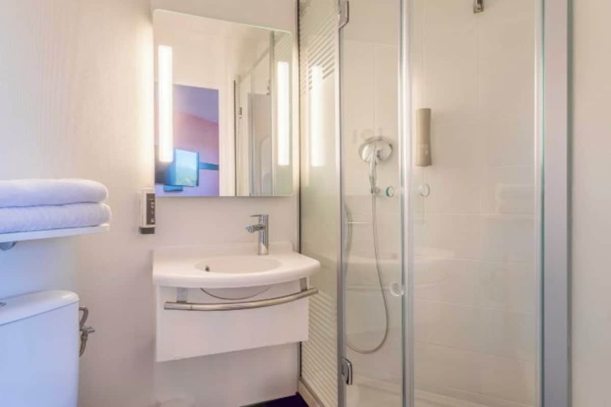 Een moderne badkamer met een douche met glazen wand, een witte wastafel en een spiegel erboven.