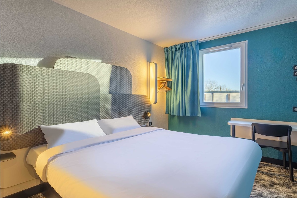 Une chambre d’hôtel avec un lit bien fait, un bureau et une chaise.