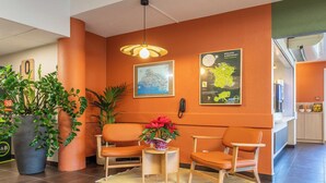 A reception area with a large potted plant, two orange chairs, a small table with a vase of flowers, and a map on the wall. - B&B HOTEL Aix-en-Provence Meyreuil Sainte-Victoire (Meyreuil)