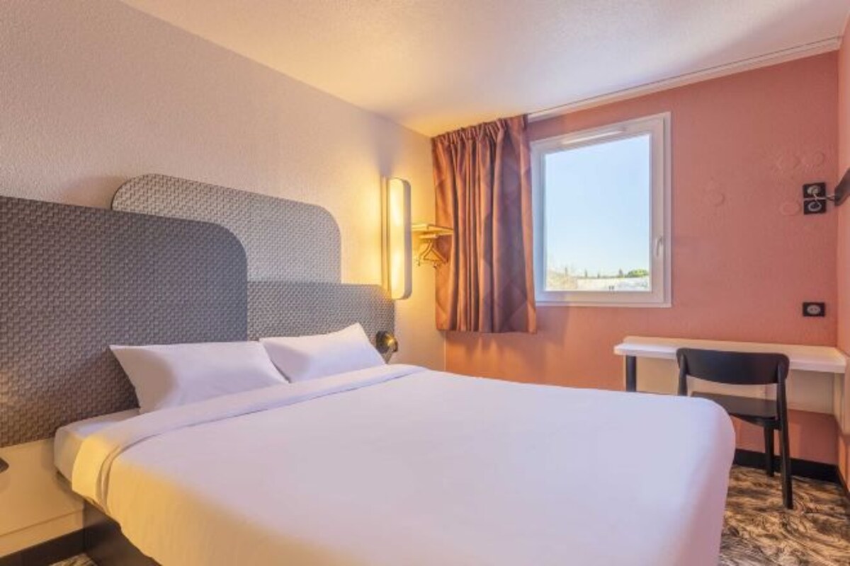 Une chambre d’hôtel avec un grand lit, un bureau et une fenêtre avec des rideaux.