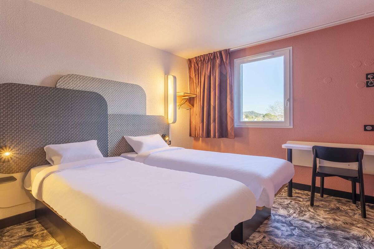 Une chambre d’hôtel avec deux lits, un bureau et une chaise.