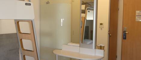 A hotel room with a bunk bed, a small bathroom with a shower, and a mirror.