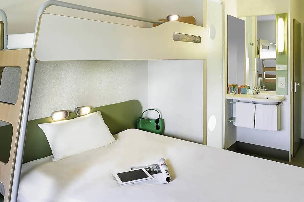 A bunk bed with a bedside table, a green handbag, a white pillow, a magazine, and a mobile phone on the bed.