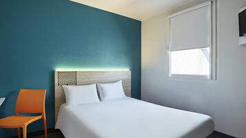 Una habitación de hotel con una cama, una silla, un ventanal y paredes color turquesa.