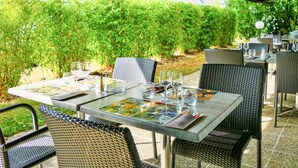 Un área de comedor al aire libre con mesas y sillas, rodeada de follaje.