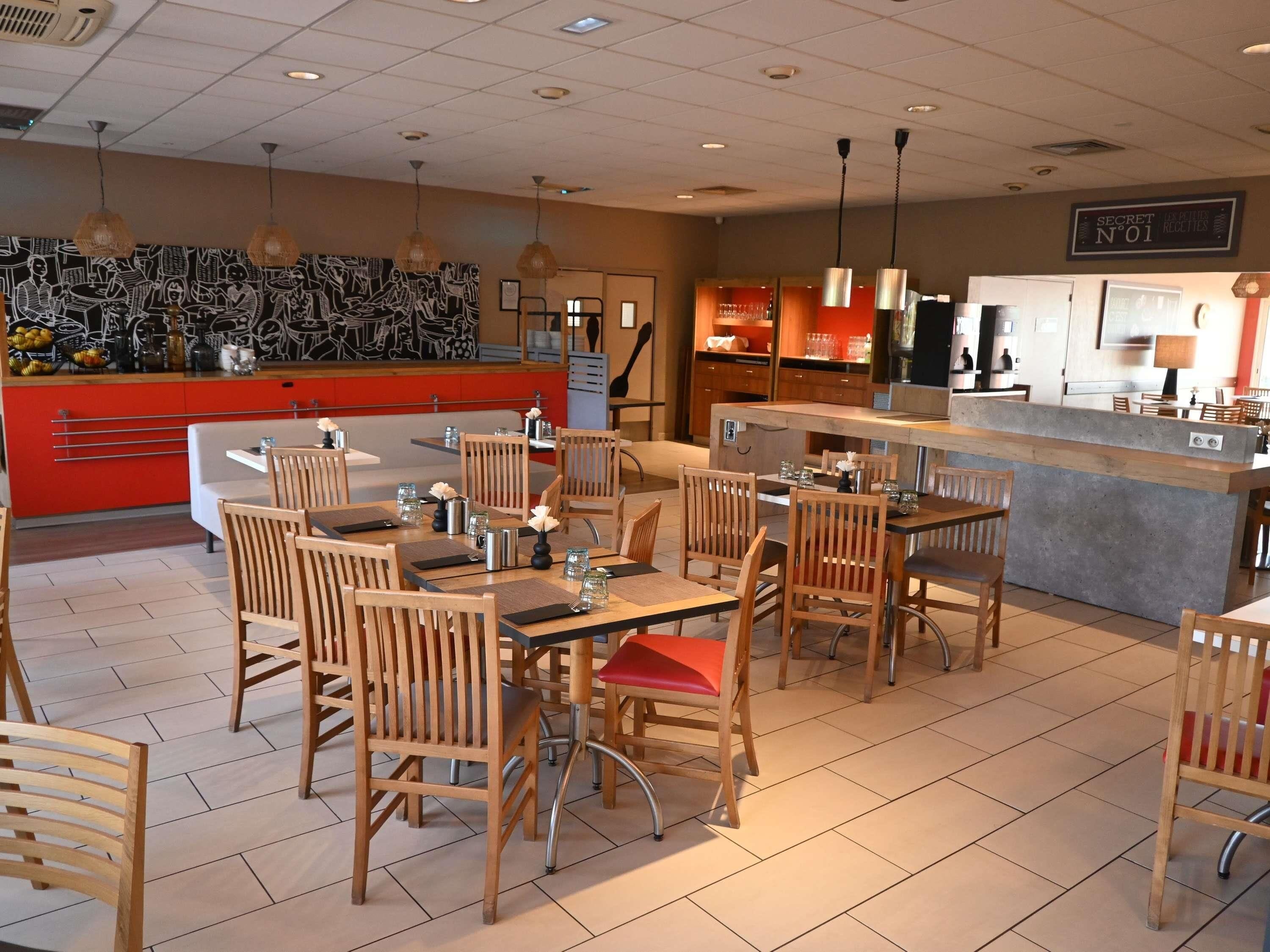 A restaurant with wooden chairs and tables, a counter, and a wall with a black and white mural.