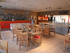 A restaurant with wooden chairs and tables, a counter, and a wall with a black and white mural.