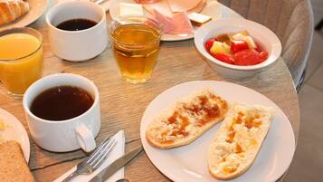 A breakfast setting with croissants, ham, cheese, fruit, and beverages on a table.