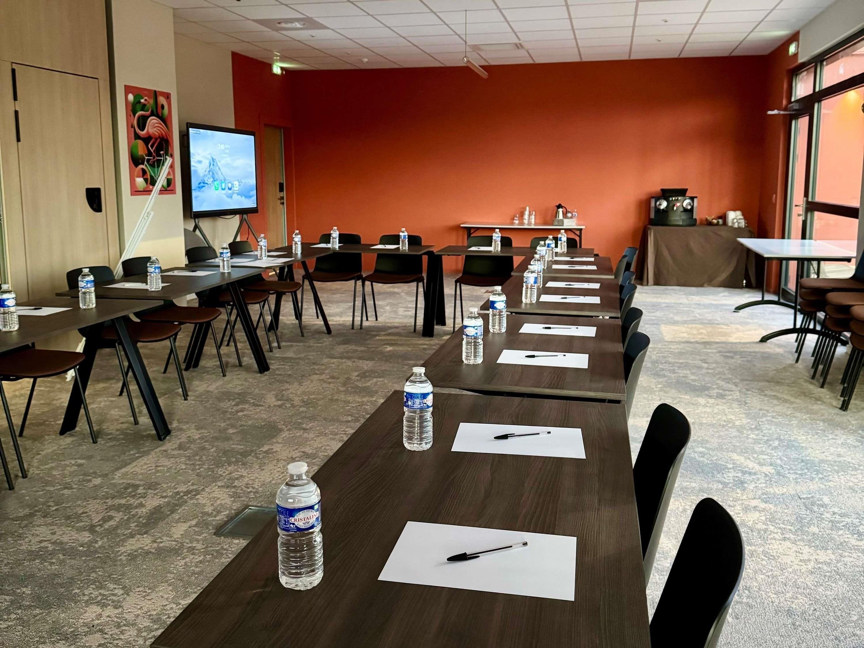 Un salón de conferencias con varias mesas, sillas, botellas de agua y una pantalla de proyector.