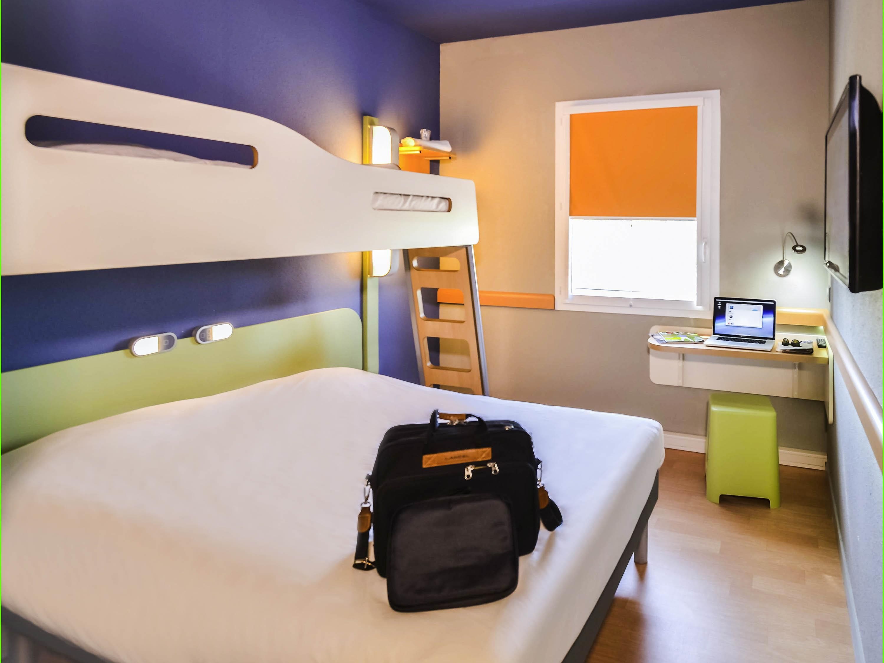 A bunk bed with a desk and a laptop, a small stool, and a bag on the bed.
