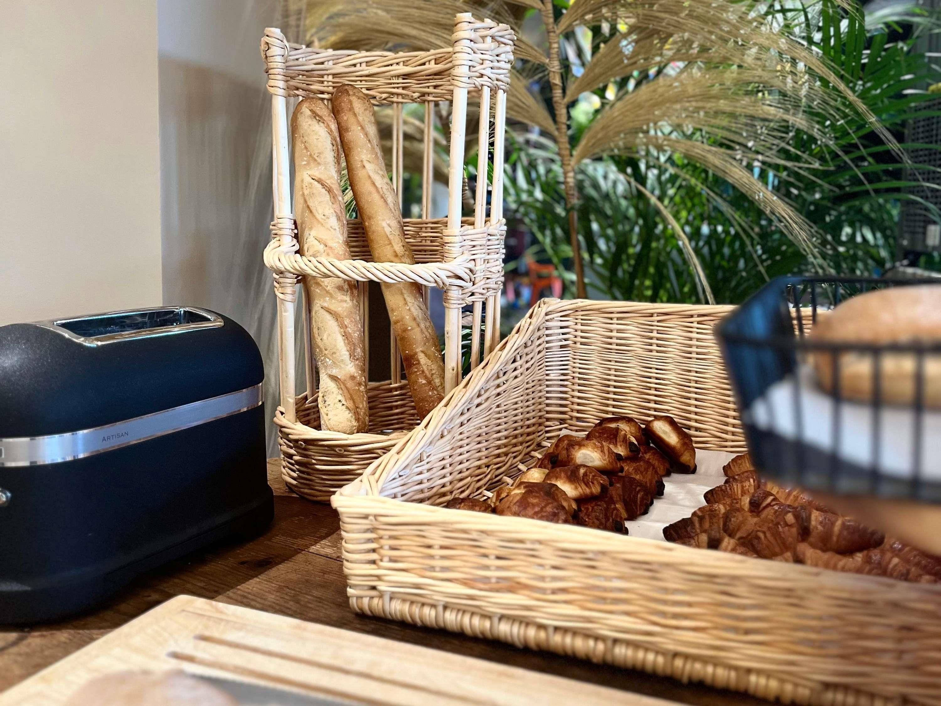 A wicker basket with baguettes and croissants on a wooden table.