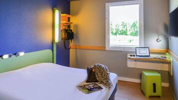 A hotel room with a bed, a desk with a laptop, a window with a view, and a bedside lamp.