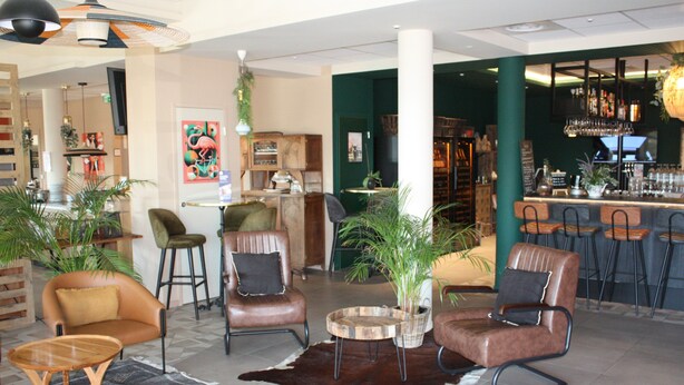 A modern lounge area with leather chairs, a bar, and a variety of plants. - ibis budget Saint Martin de Crau Porte de Camargue (Saint-Martin-de-Crau)