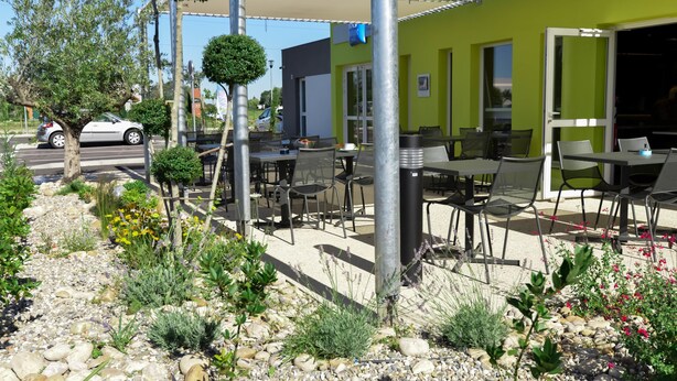 An outdoor seating area with tables and chairs, surrounded by a garden with various plants and a gravel path. - ibis budget Saint Martin de Crau Porte de Camargue (Saint-Martin-de-Crau)