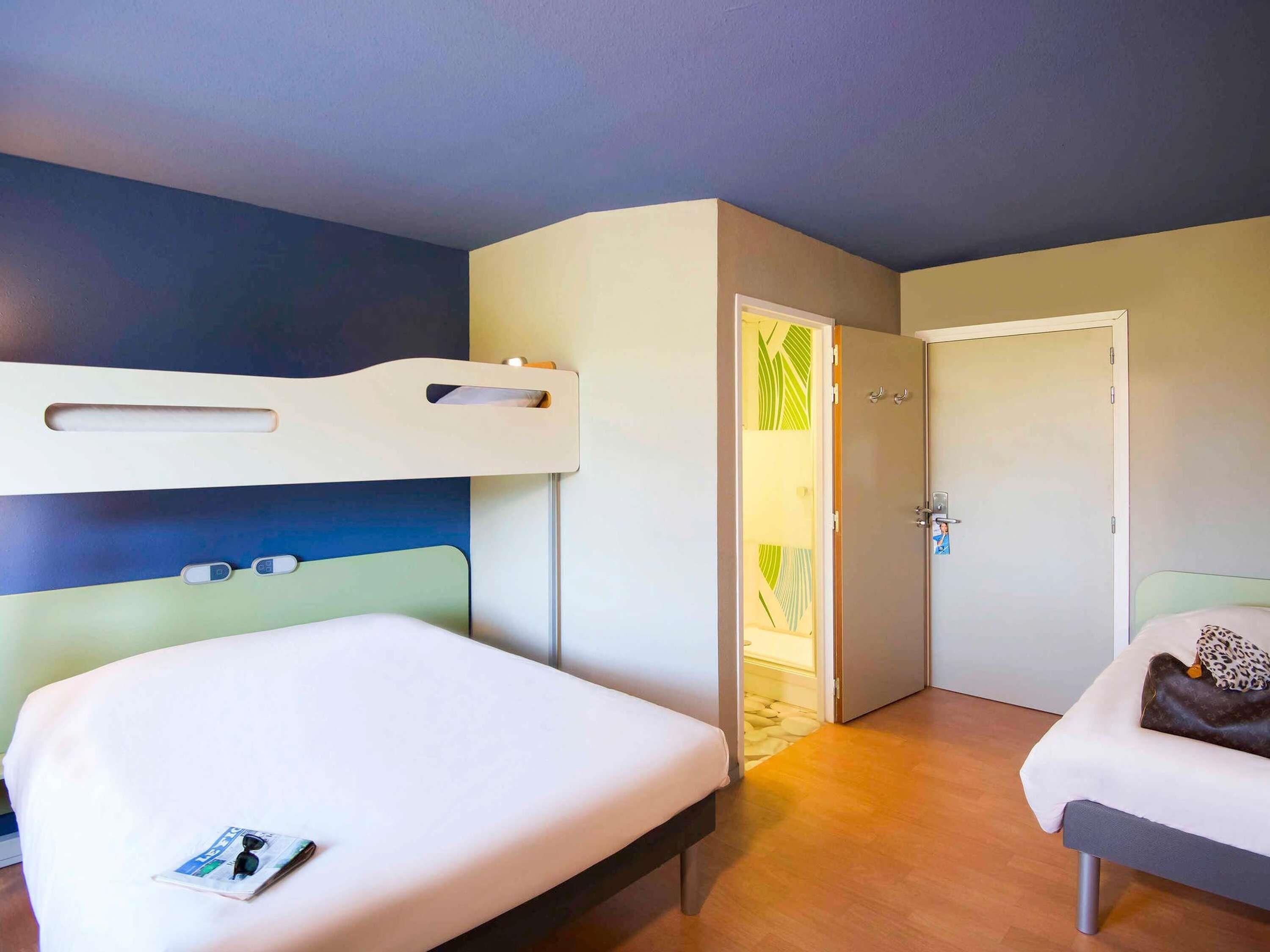 Ein Hotelzimmer mit zwei Betten, einem Etagenbett, einer Tür mit einem grün gemusterten Vorhang und einer Wand mit blaugrünem Dekor.