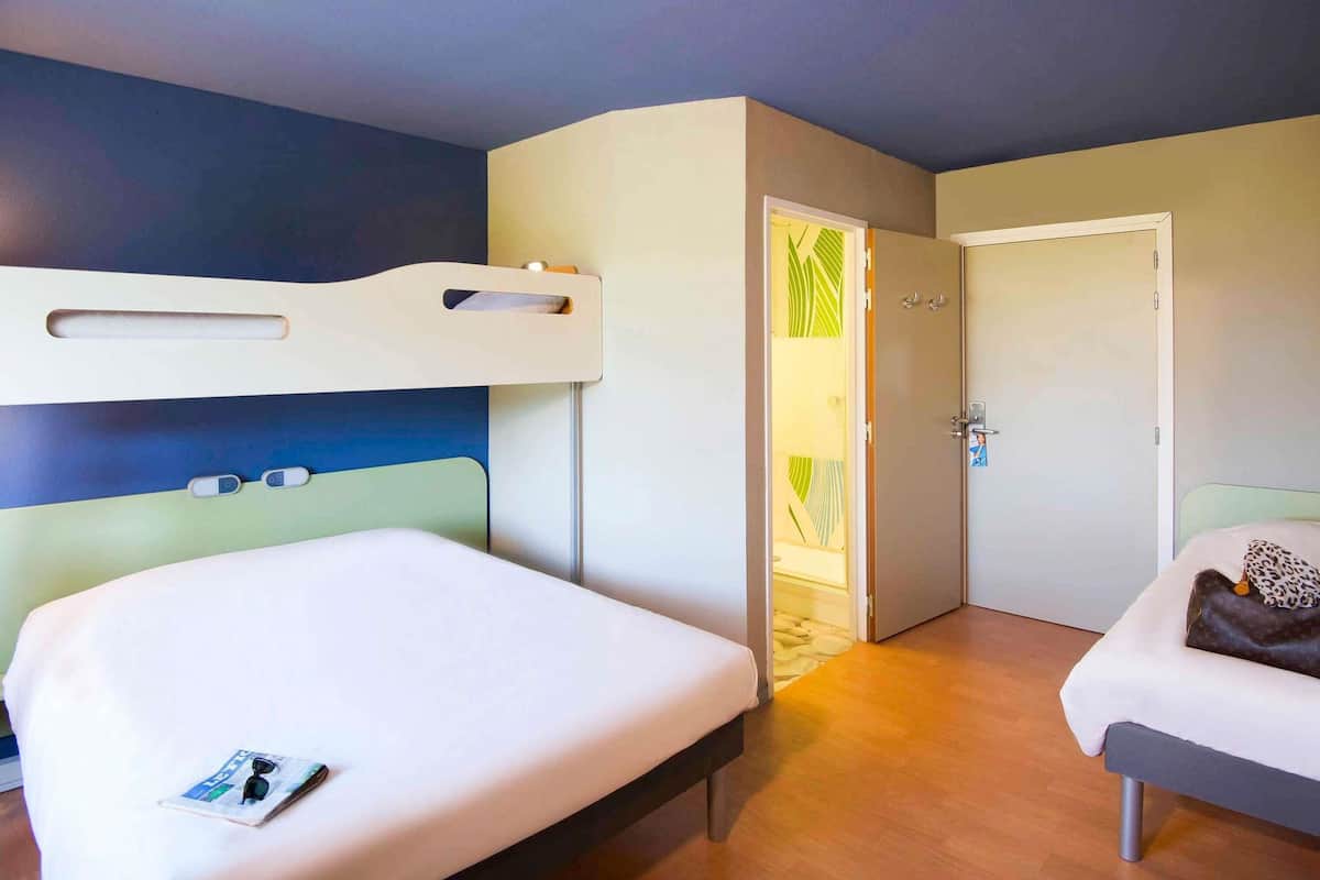 Ein Hotelzimmer mit zwei Betten, einem Etagenbett, einer Tür mit einem grün gemusterten Vorhang und einer Wand mit blaugrünem Dekor.