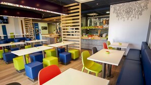 A modern restaurant with colorful seating and a visible kitchen area. - ibis budget Saint Martin de Crau Porte de Camargue (Saint-Martin-de-Crau)