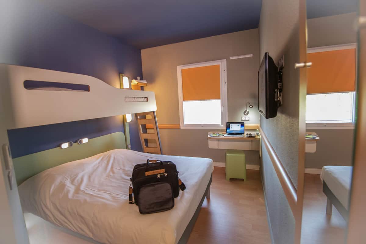 A bedroom with a bunk bed, a desk with a laptop, and a window with blinds.