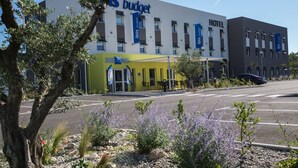 A modern hotel building with "Ibis Budget" signage, outdoor seating, and a parking lot. - ibis budget Saint Martin de Crau Porte de Camargue (Saint-Martin-de-Crau)
