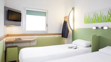 Habitación de hotel con cama, escritorio con silla, televisor montado en la pared y ventana con vistas.