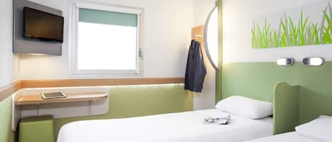 Habitación de hotel con cama, escritorio con silla, televisor montado en la pared y ventana con vistas.