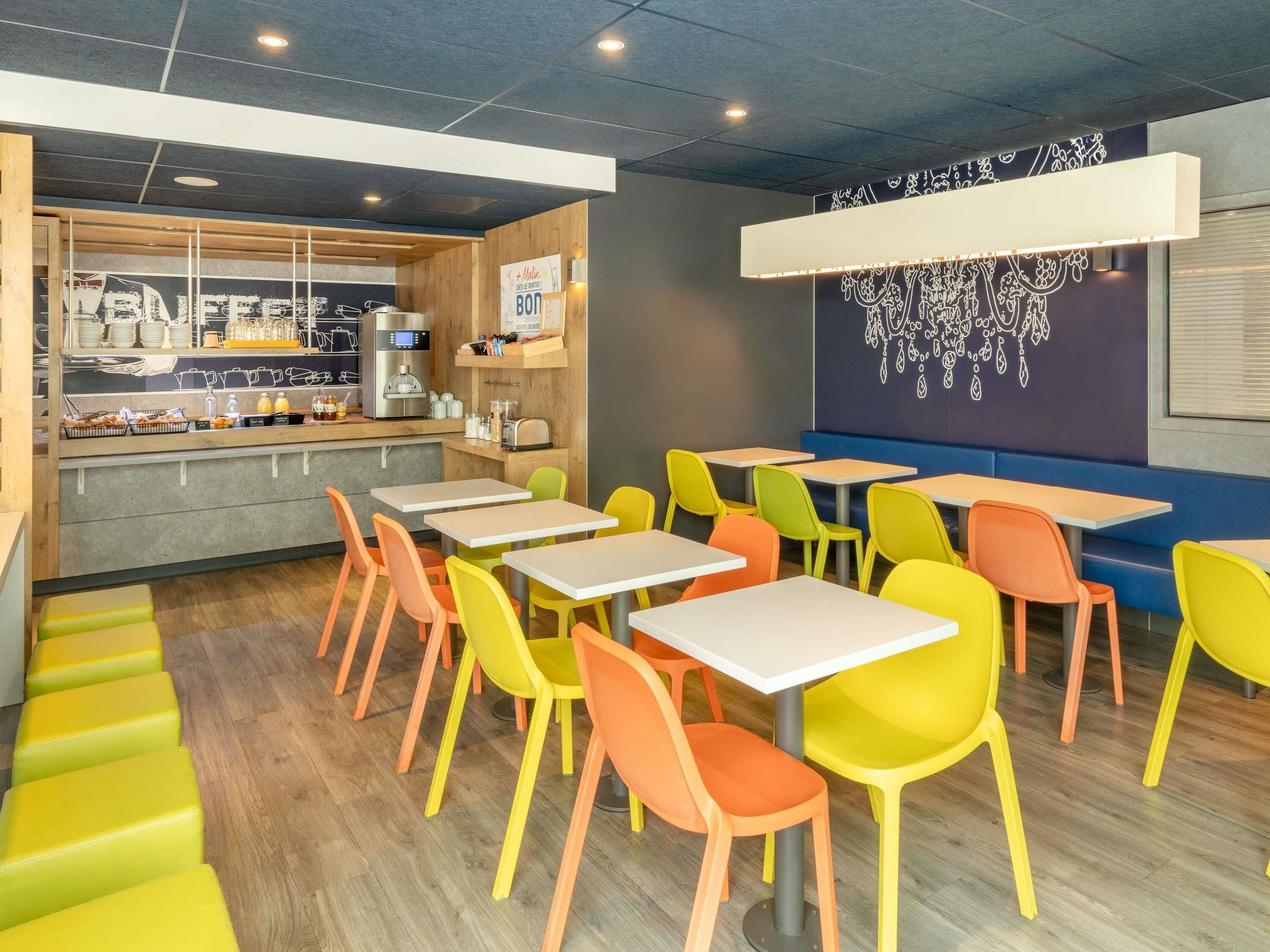 A restaurant with colorful chairs and tables, a counter with food items, and a wall with a decorative pattern.