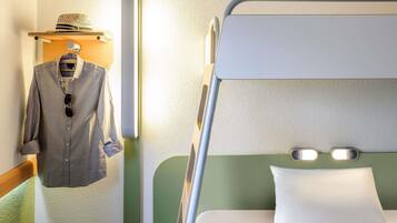 A bunk bed with a green headboard, a hanging shirt rack with a hat, and a bedside table with a lamp.