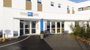 Een moderne hotelentree met een blauw bord, glazen deuren en een terras.