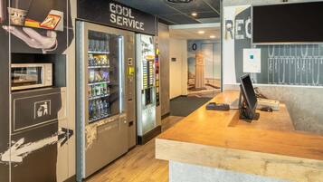 A coffee service area with vending machines, a reception desk, and a view of a clock tower through a glass wall.