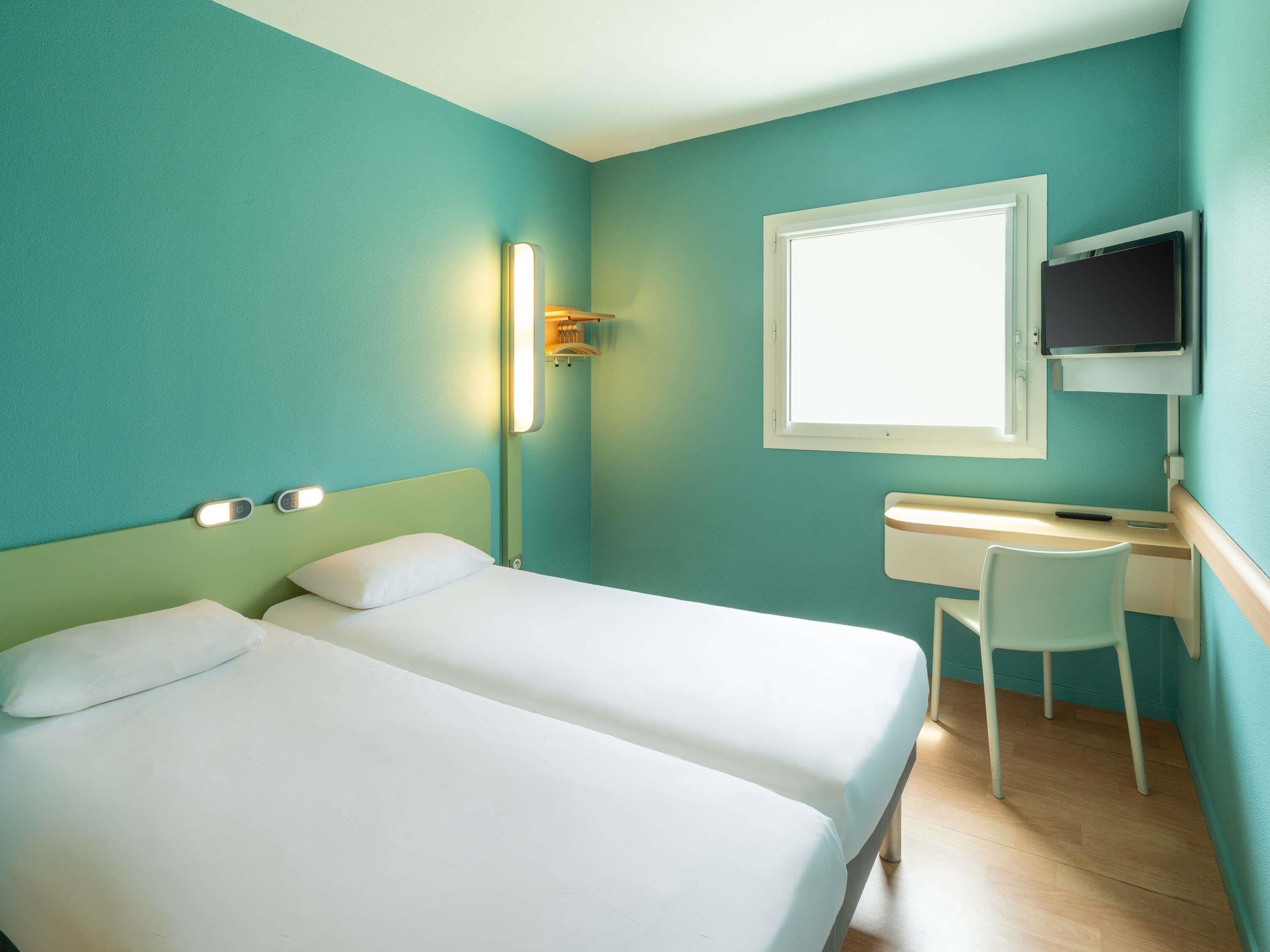 Habitación de hotel con dos camas, un escritorio, una silla, un televisor y una ventana.