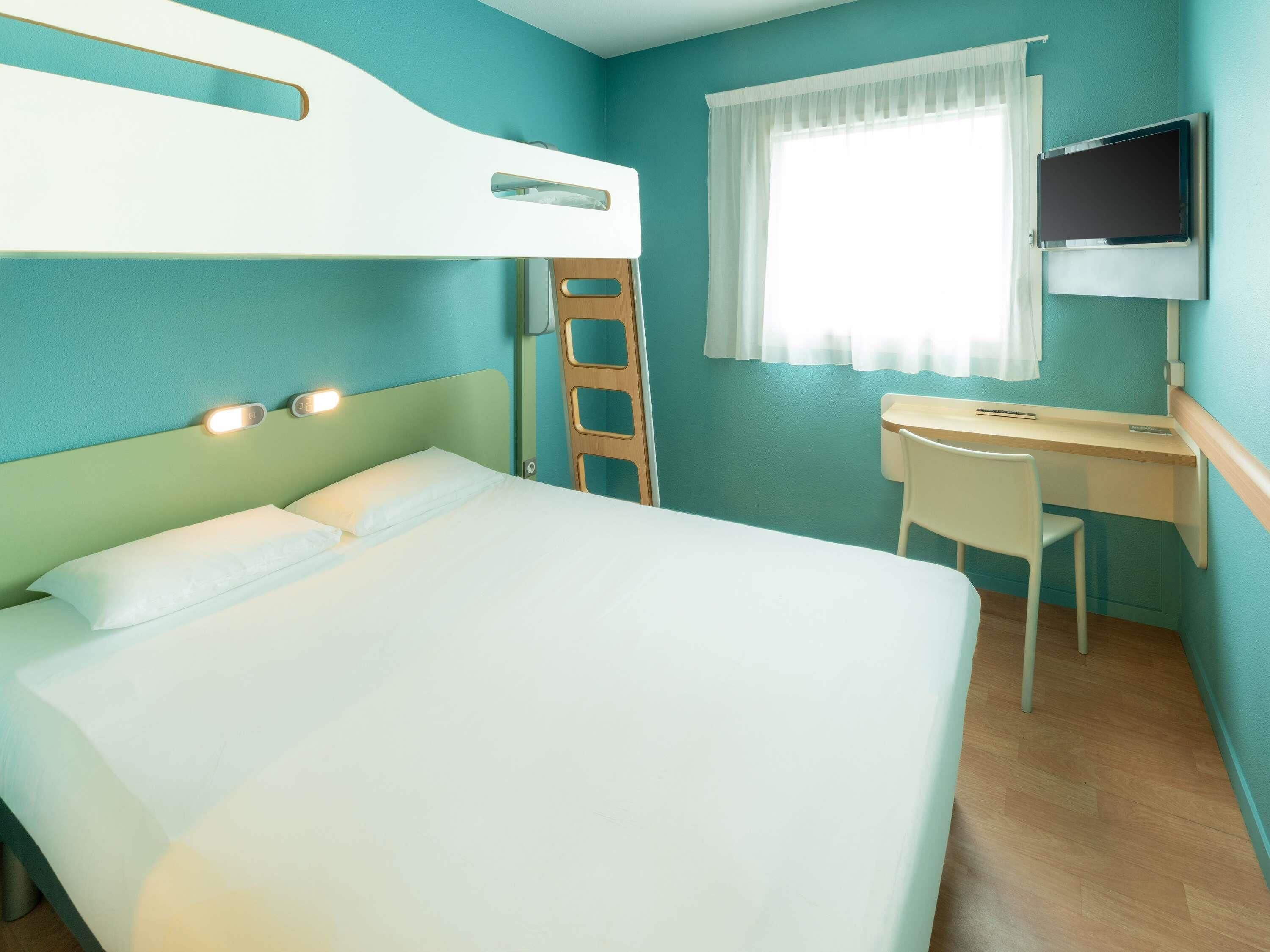 A hotel room with a bed, a desk, a chair, a television, and a window with curtains.