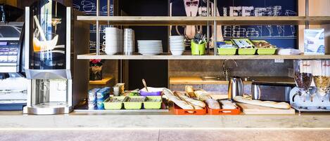 Mostrador de cafetería con una máquina de café, diferentes productos alimenticios y una exposición de tazas de café.