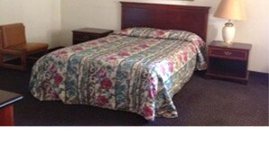 Une chambre d’hôtel avec un lit, une chaise, une table de chevet, une lampe et un tableau au mur.