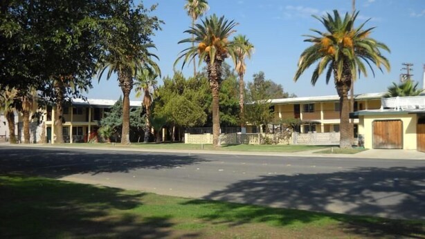 Un motel à deux étages avec une cour intérieure, des palmiers et un ciel dégagé.