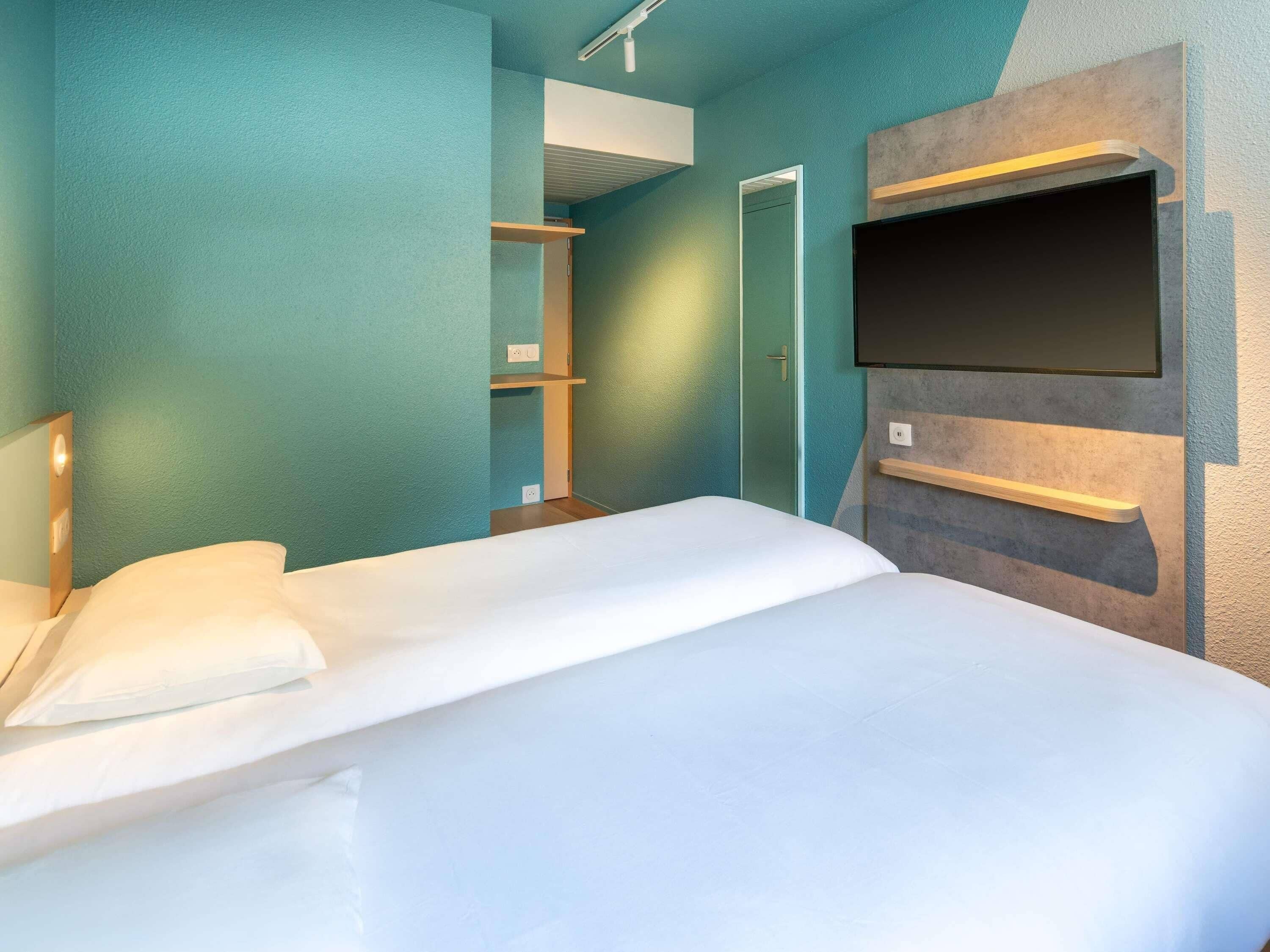 Una habitación de hotel moderna con una cama grande, un televisor de pantalla plana en la pared y un vestidor.