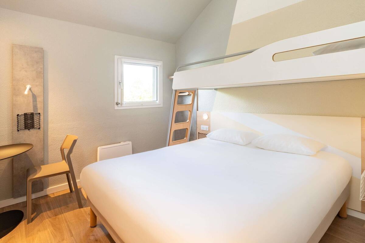 Une chambre avec un lit superposé, un bureau avec une chaise, une petite fenêtre et un radiateur.