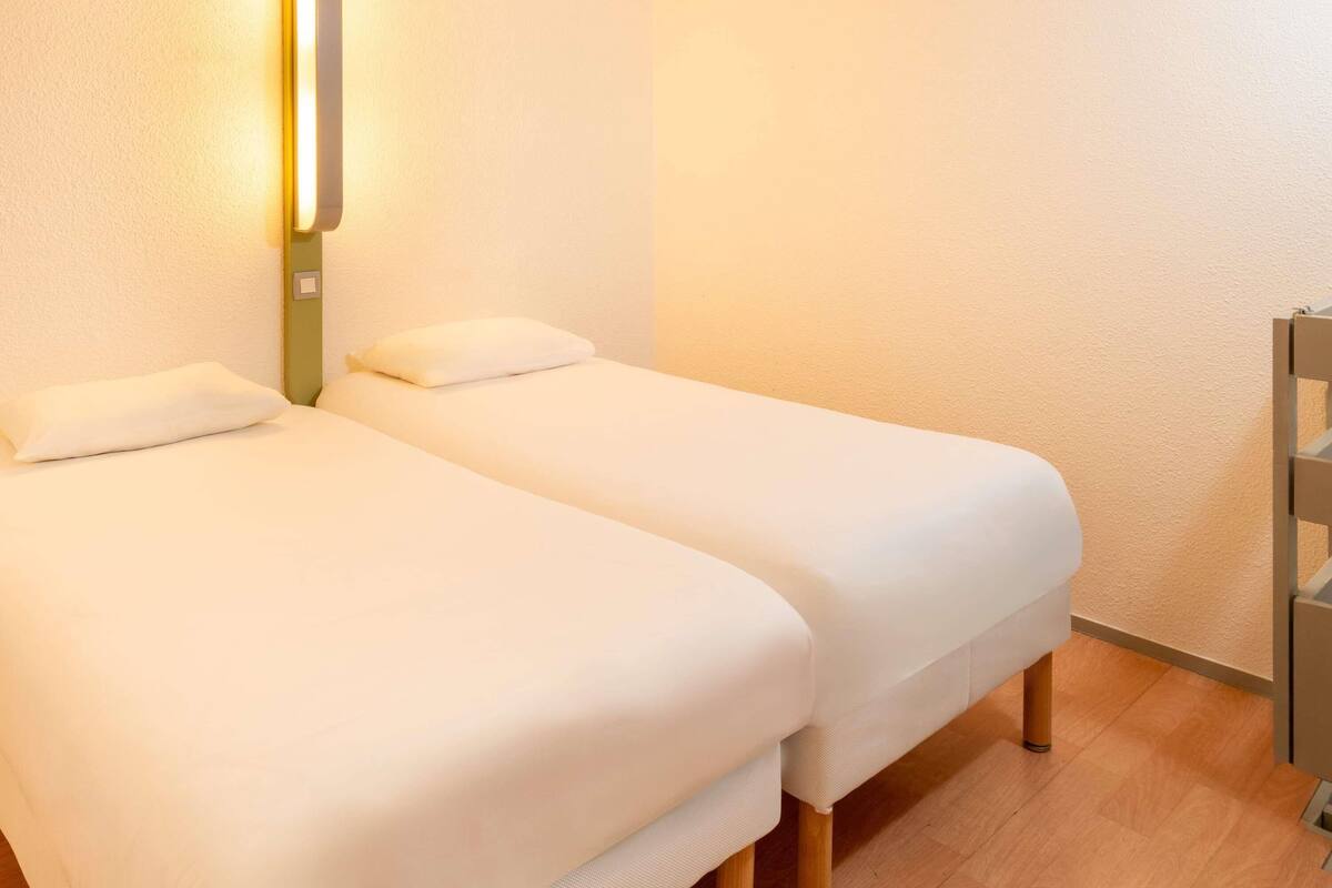 Une chambre avec deux lits, un luminaire fixé au mur et un plancher en bois.
