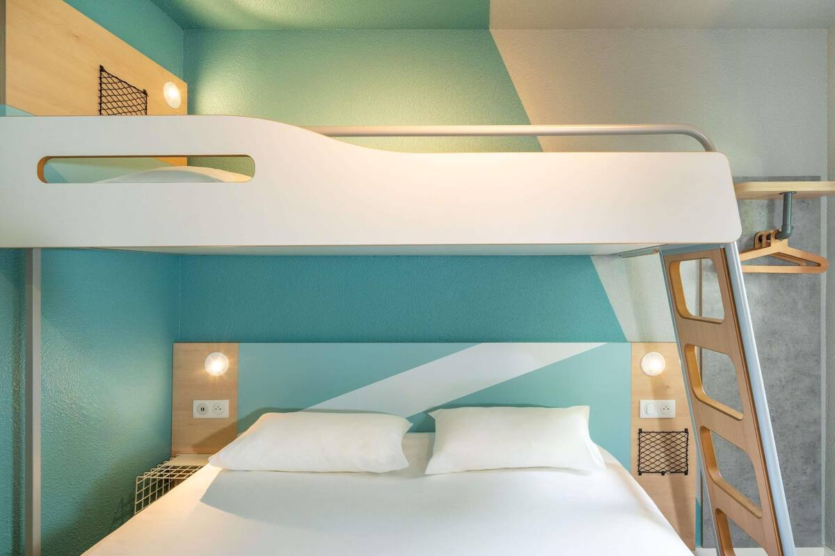Un lit superposé avec une échelle, une table de chevet et un luminaire fixé au mur.