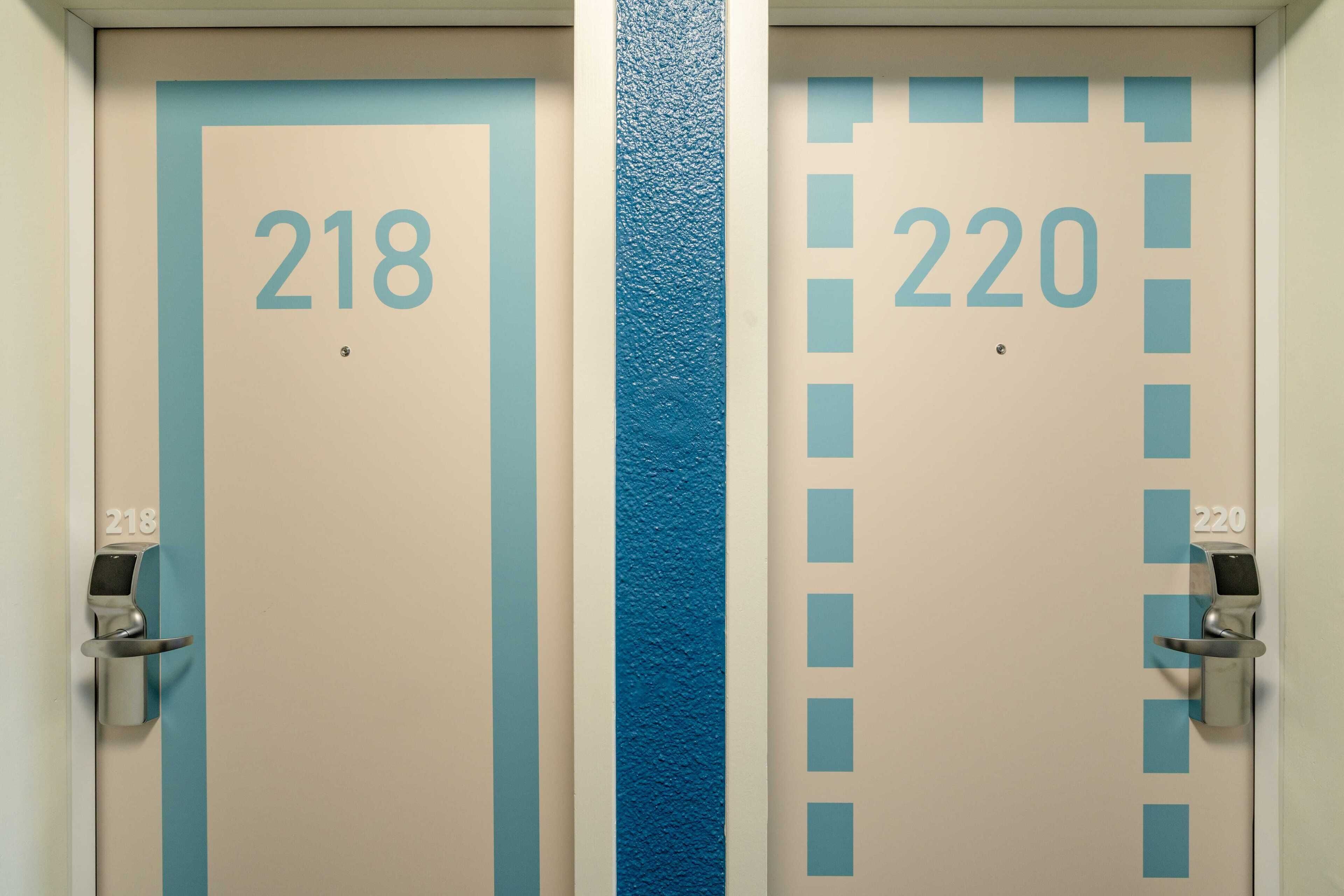Dos puertas, una con la etiqueta 218 y la otra con la etiqueta 220, con una franja azul en el medio.