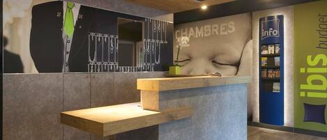 A reception desk with a modern design, a wall with a large 'CHAMBRES' sign, and a bookshelf labeled 'info budget'.
