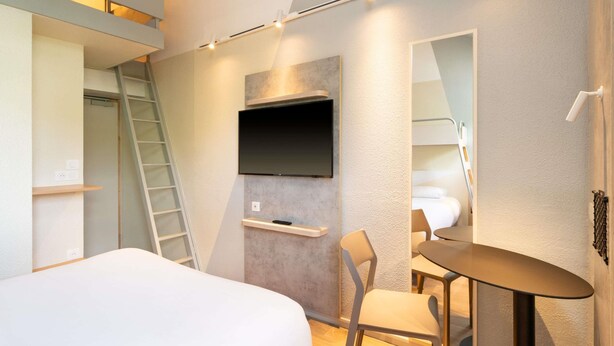 Ein modernes Hotelzimmer mit Bett, Schreibtisch, Stuhl, Wandfernseher und einer Leiter.