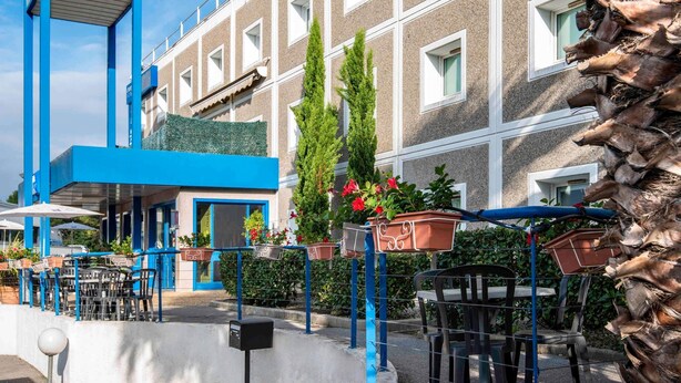 An ibis budget hotel with a blue and white facade, outdoor seating area, and potted plants. - ibis budget Antibes Sophia Antipolis (Vallauris)
