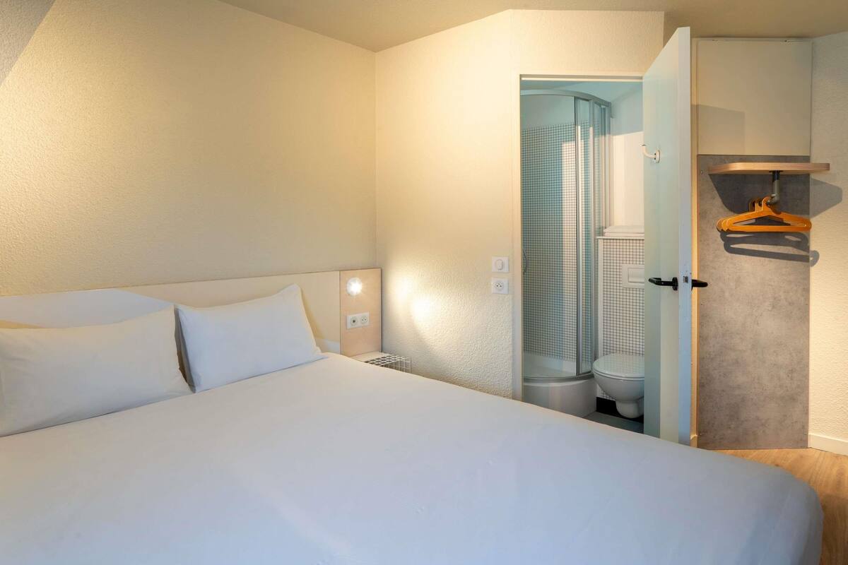 Hotellihuone, jossa on suuri sänky, suihkutila sekä pieni oleskelualue, jossa on tuoli ja pöytä.