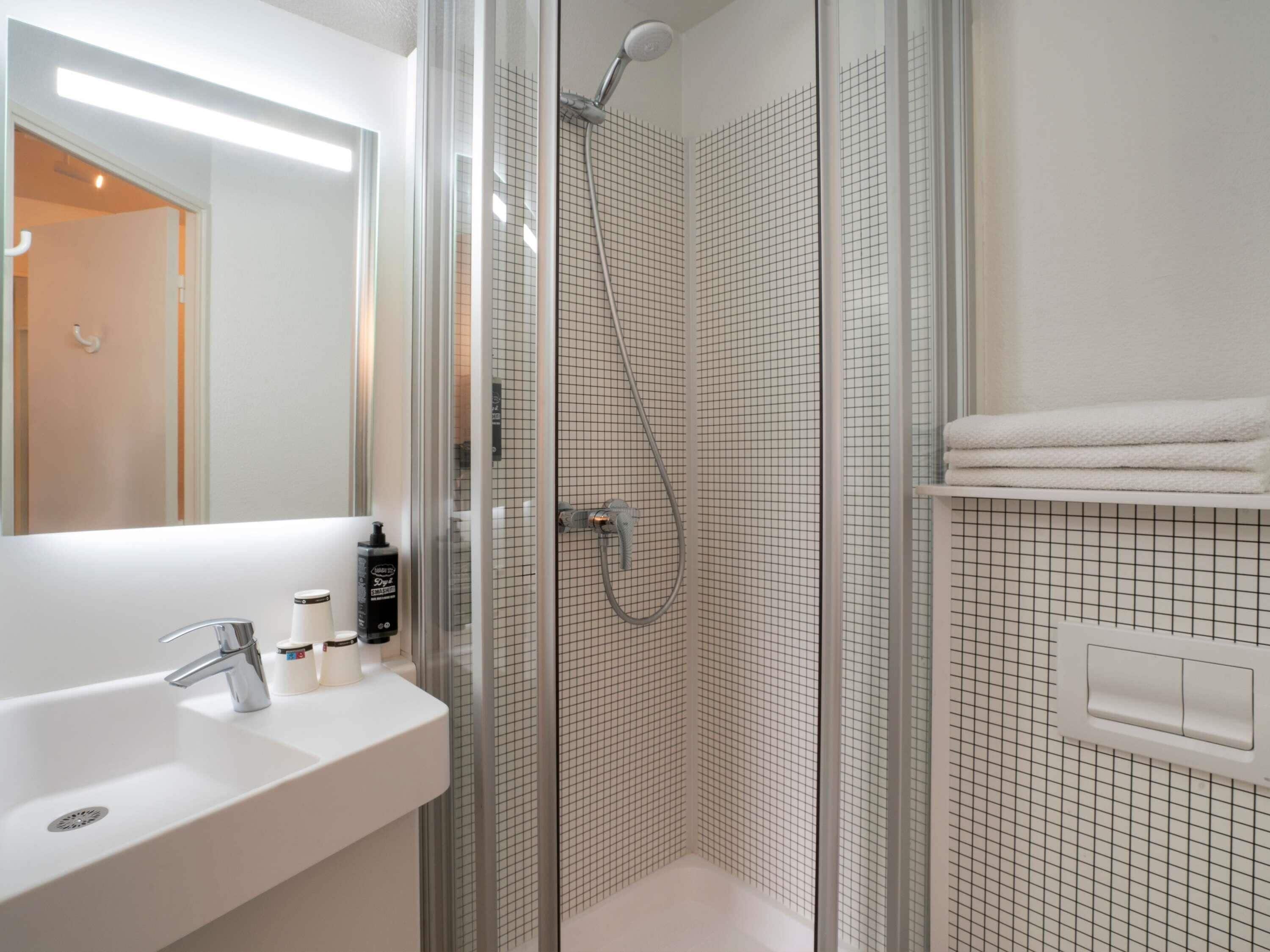 Une salle de bain moderne avec une douche à parois de verre, un lavabo blanc et un miroir.