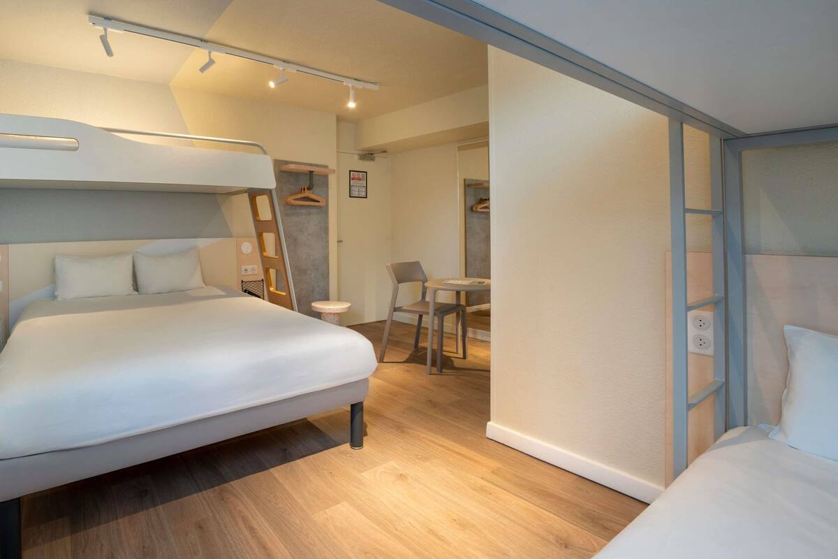 Moderni hotellihuone, jossa on kerrossänky, pieni pöytä, tuoli ja työpöytä.