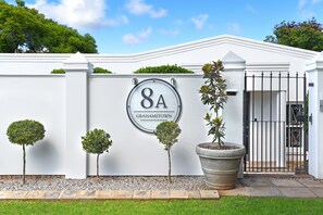 A white building with a sign reading "8A GRAHAMSTOWN" and a gated entrance. - 8A Grahamstown (Makhanda)
