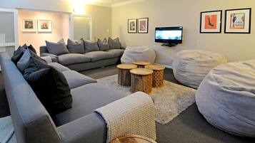 Una sala de estar con un sofá gris, un sillón gris, una mesa de centro redonda de madera, un asiento tipo saco y un televisor de pantalla plana montado en la pared.