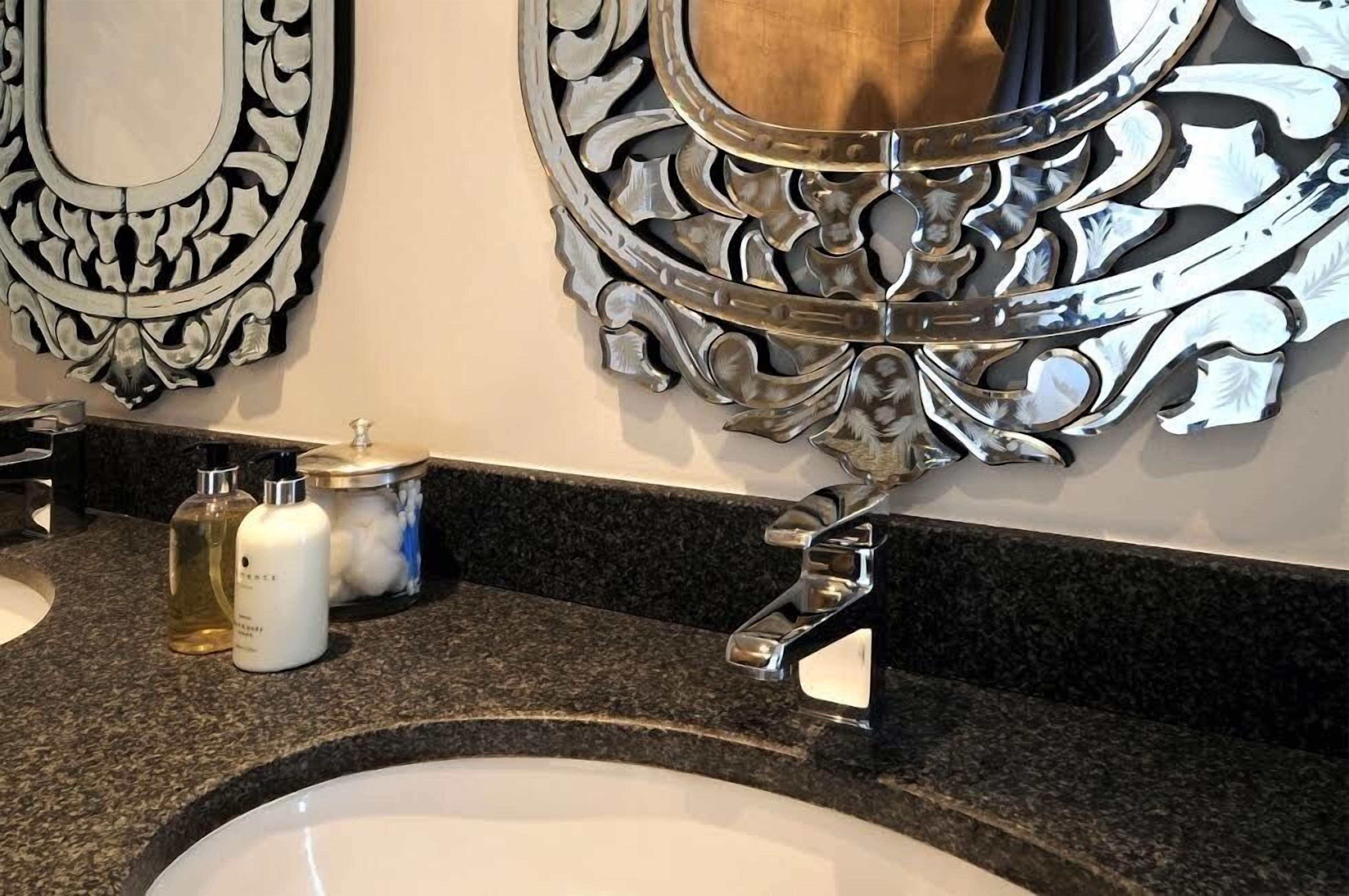 A bathroom with a granite countertop, two sinks, and ornate wall mirrors.